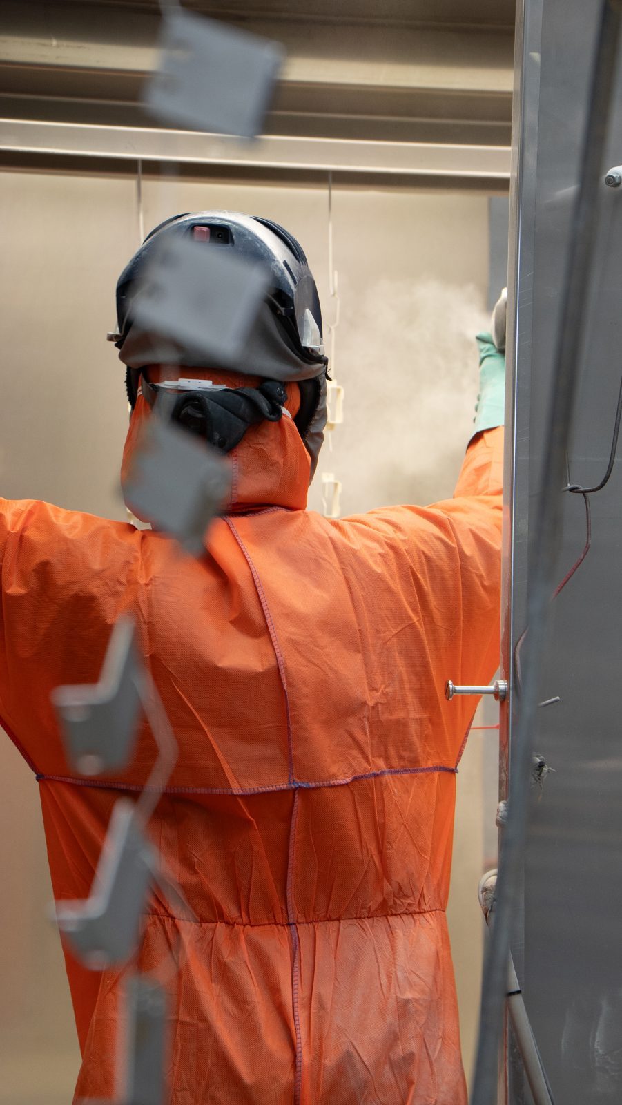 Operator powder coating a steel part in the spray booth